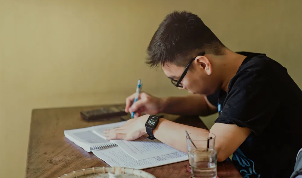 Joven con lentes estudia y subraya en su cuaderno