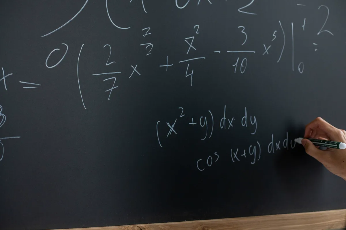 Mano escribiendo una integral con plumón sobre una pizarra oscura