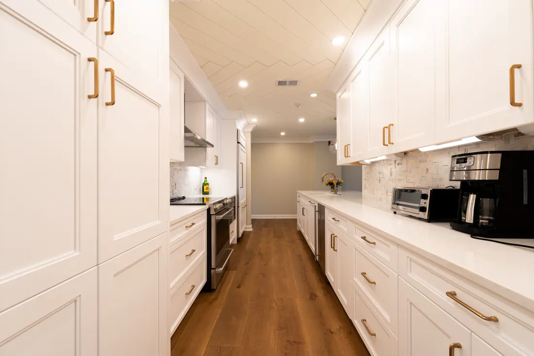 Cocina en línea con muebles blancos, tiradores dorados y piso de madera
