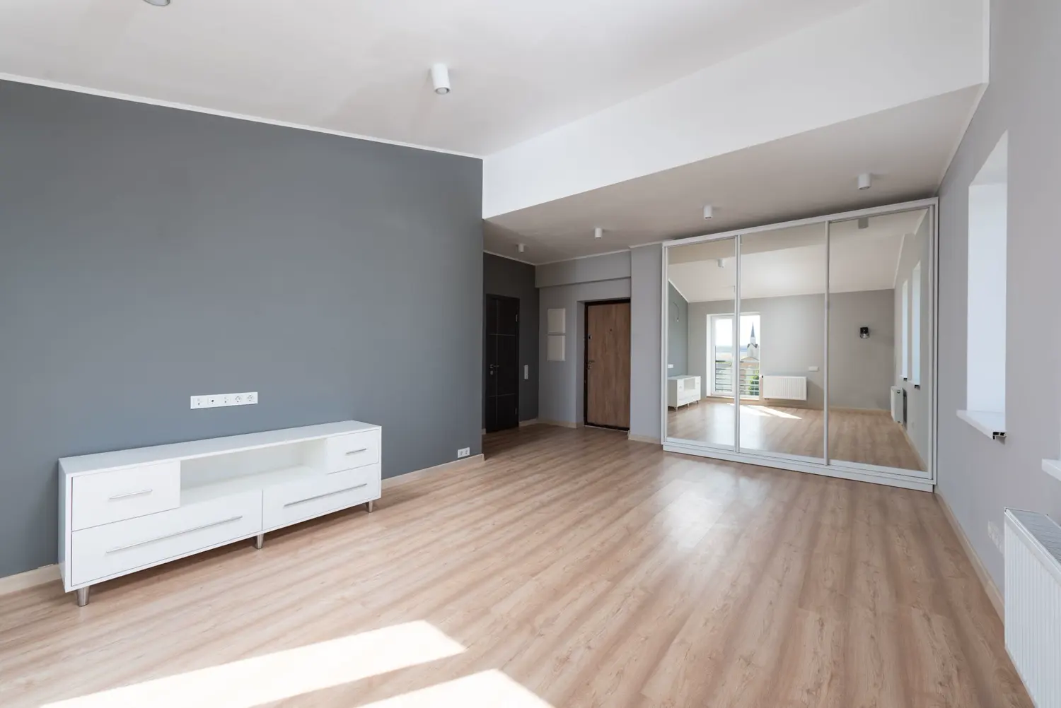 Sala amplia con muro gris y piso laminado claro