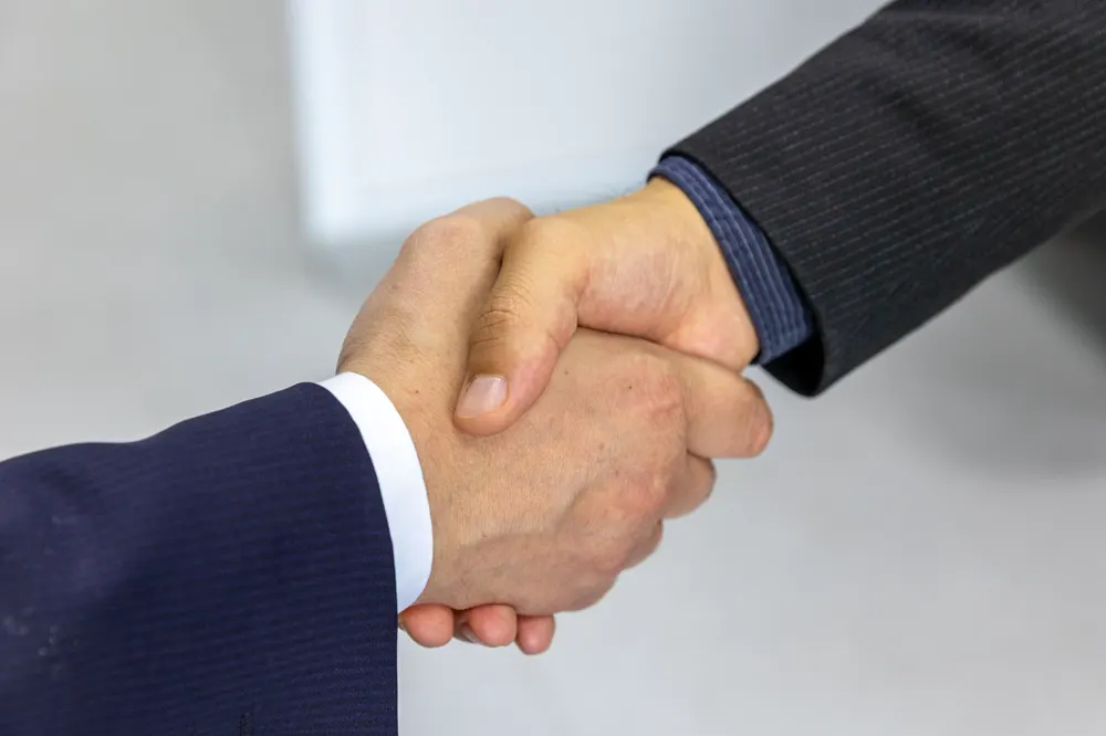 Dos personas se dan la mano sobre un fondo claro